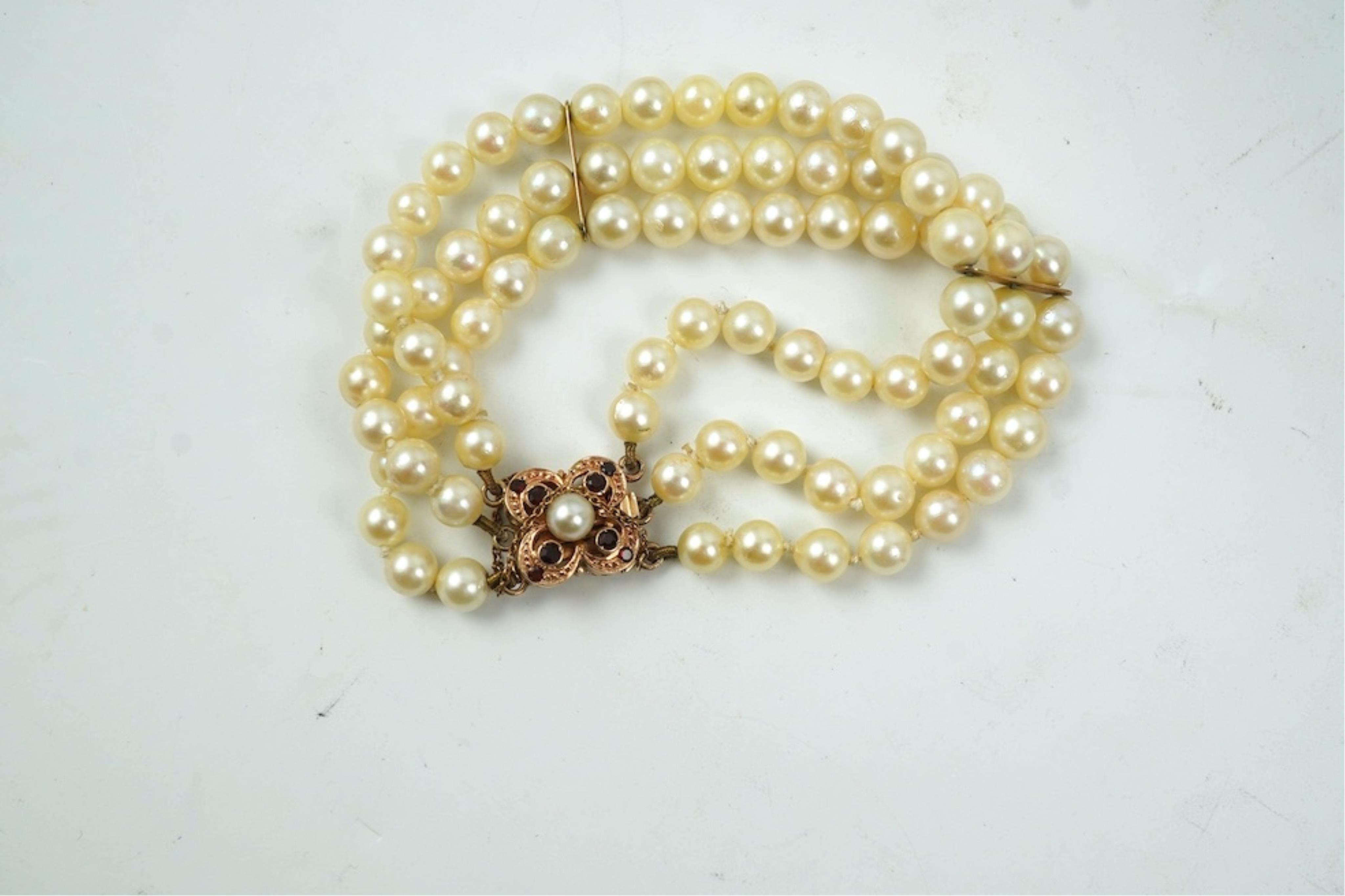 A triple strand cultured pearl bracelet, with a 9ct gold, garnet and cultured pearl cluster set clasp, 16cm.